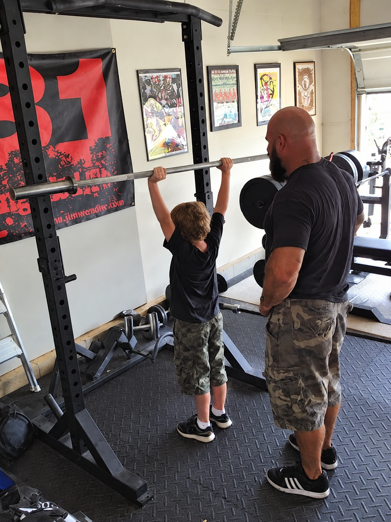 Jim teaching his son Mason the barbell overhead press in the garage gym