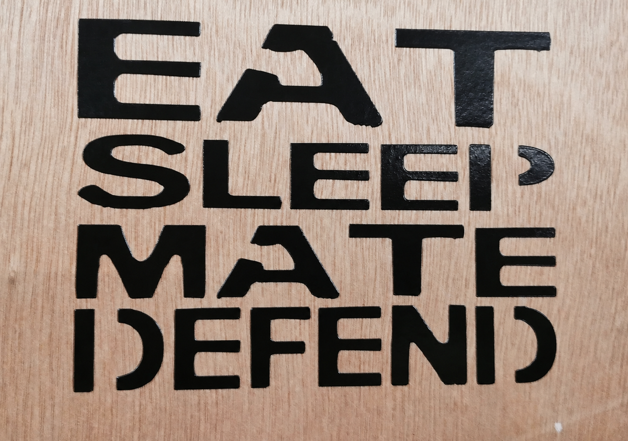 Black Eat Sleep Mate Defend transfer decal applied directly to a wood surface.
