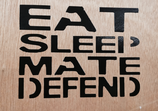 Black Eat Sleep Mate Defend transfer decal applied directly to a wood surface.
